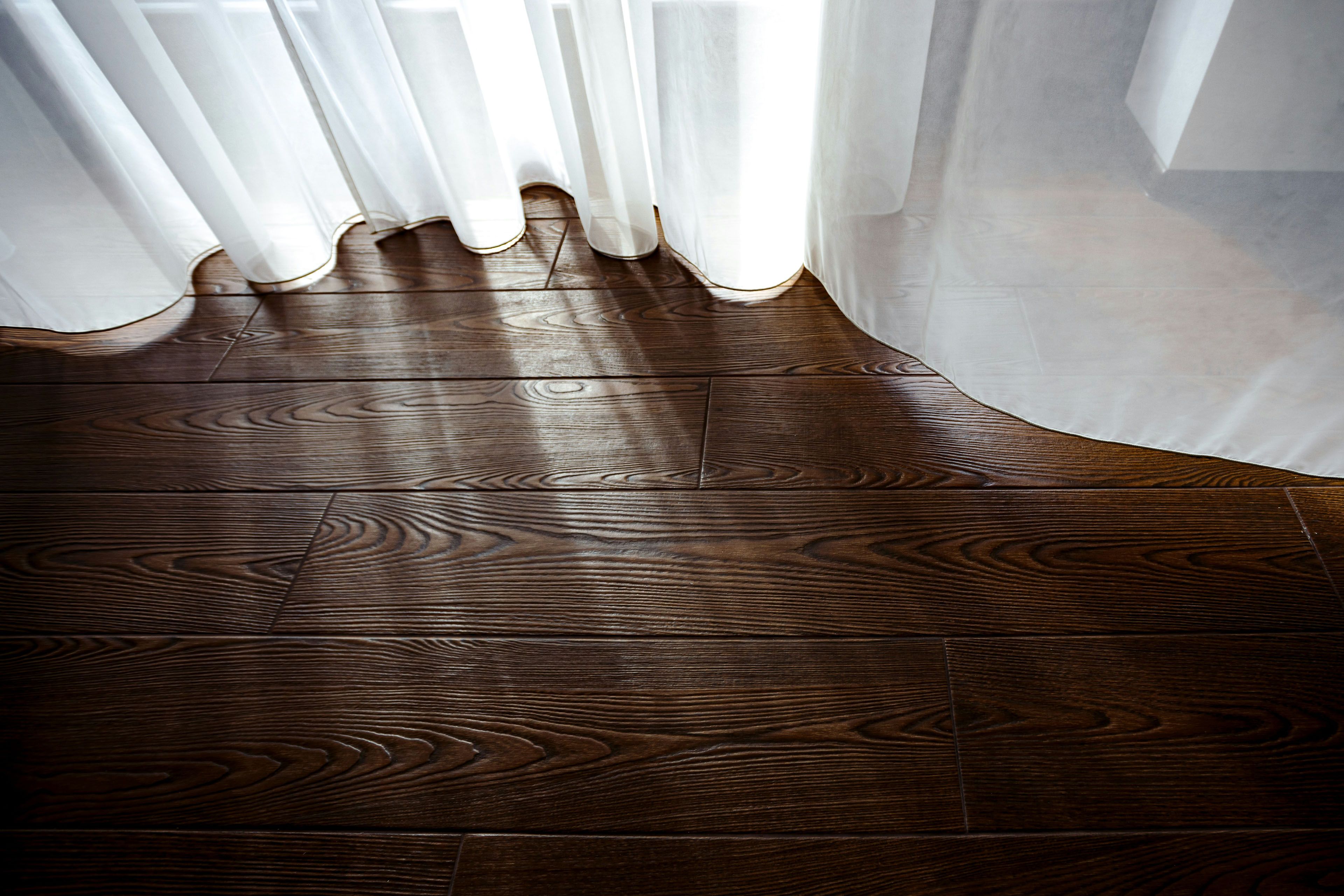 Dark wood floors with sunlight shining through the white curtains